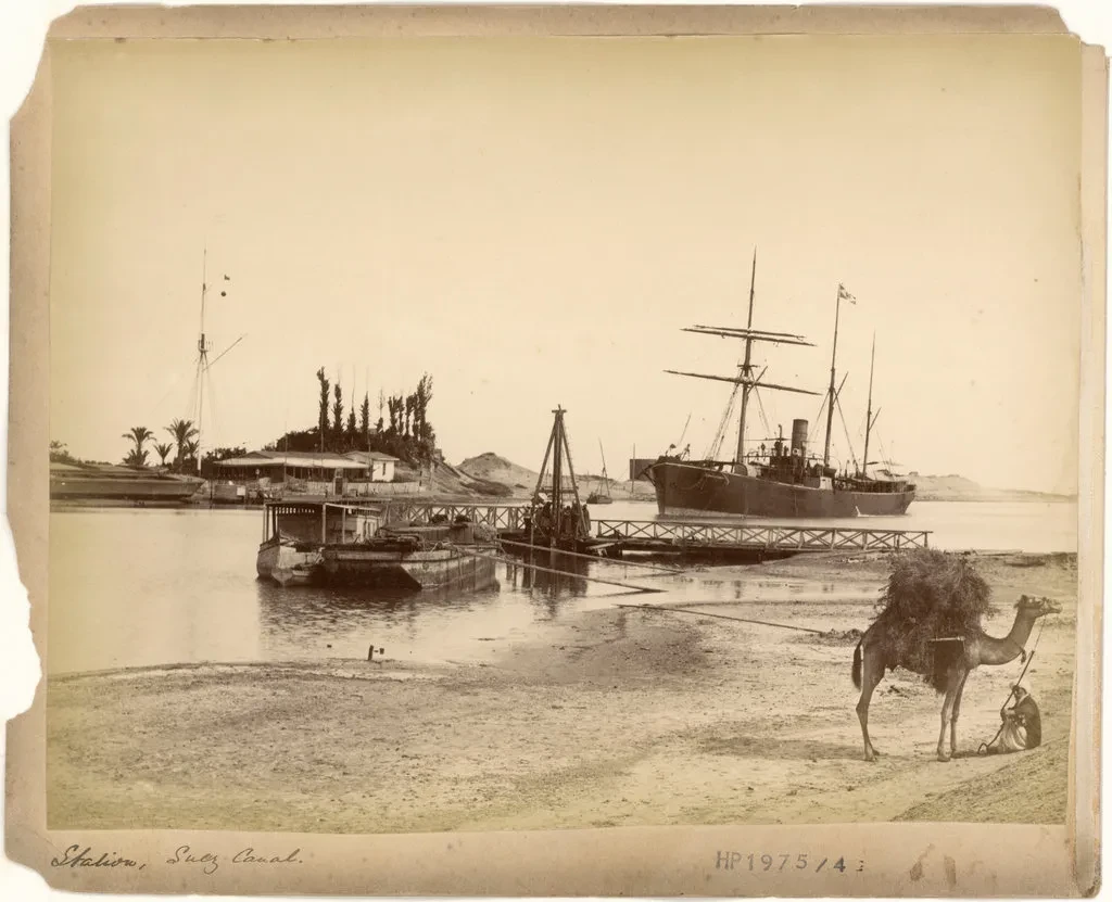 Historic sepia-toned photograph showing a ship on the Suez Canal. A camel is in the foreground