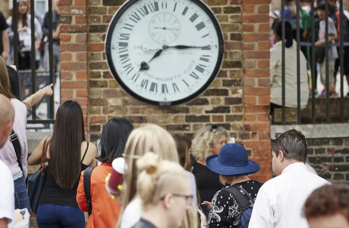 A crowd looking at the Shepherd Gate Clock on a brick wall. 
