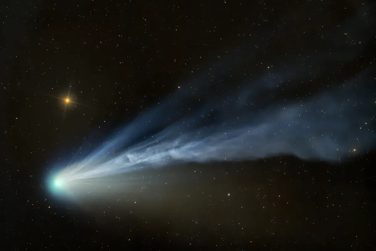 A bright blue comet with a long cloud-like tail in a black, starry sky.