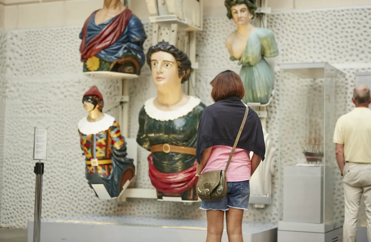 Visitors look at figureheads on display.