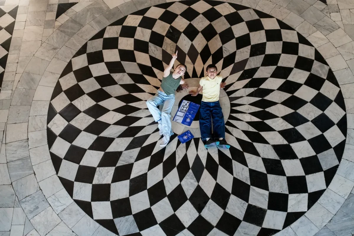 A girl and boy lie in the middle of the Great Hall of the Queen's House, looking up at the ceiling