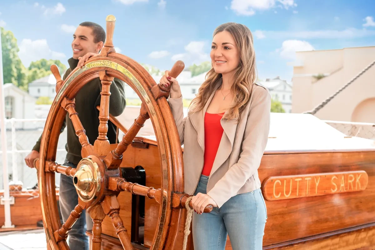 A man and a woman hold the ship's wheel on board Cutty Sark