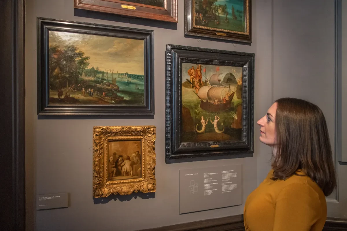 A woman wearing a yellow jumper gazes at paintings in an art gallery