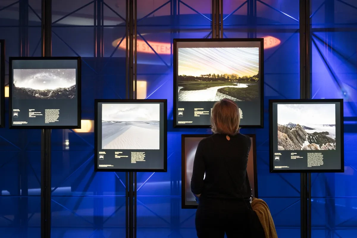 A woman, with her back to the camera, looks at a number of astronomy photographs lit up on large illuminated display screen