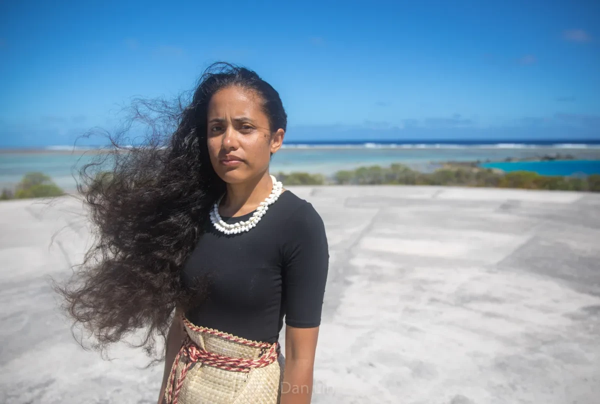 Image of a woman wearing a black t shirt standing on a beach with a bright blue sky