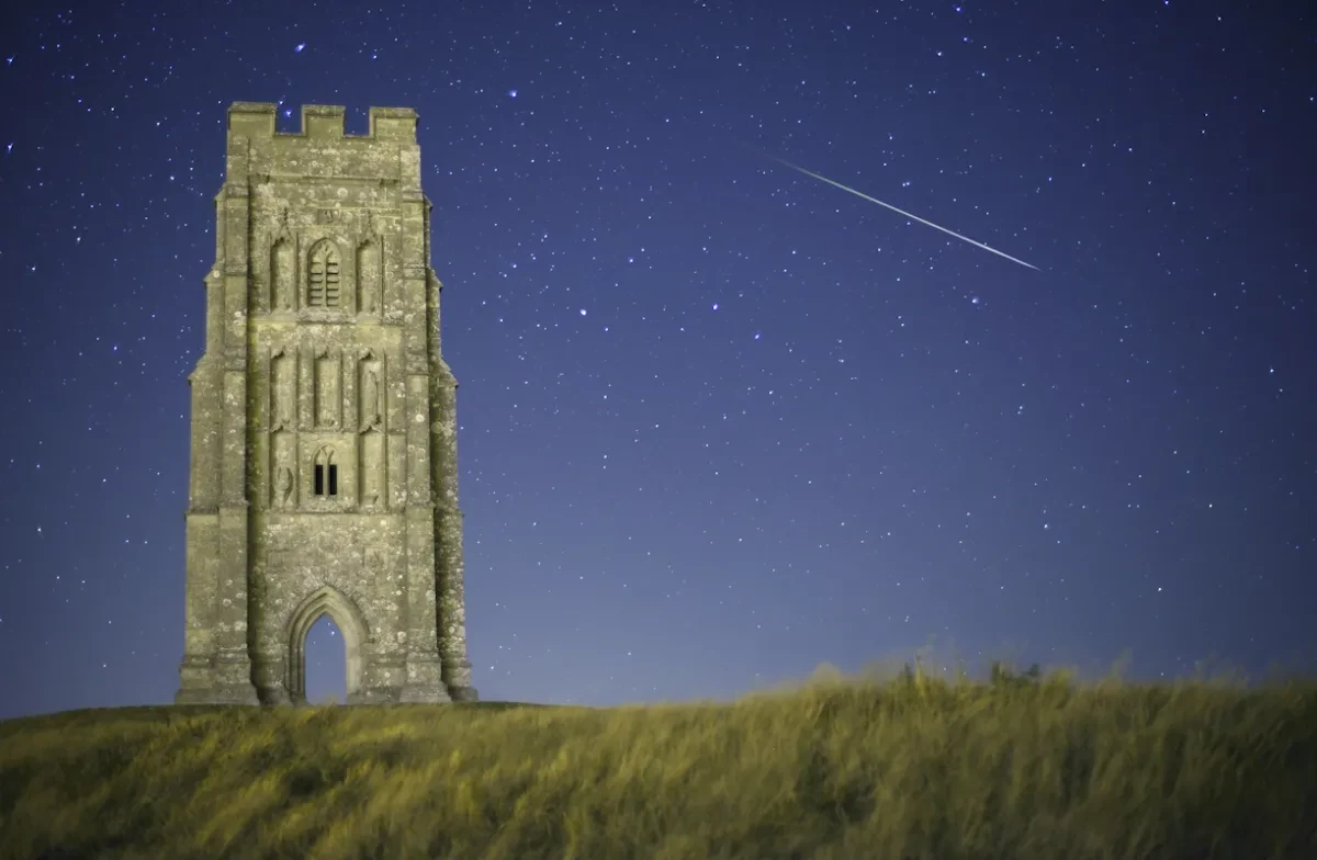 Photograph of a meteor in the night sky above a tower.