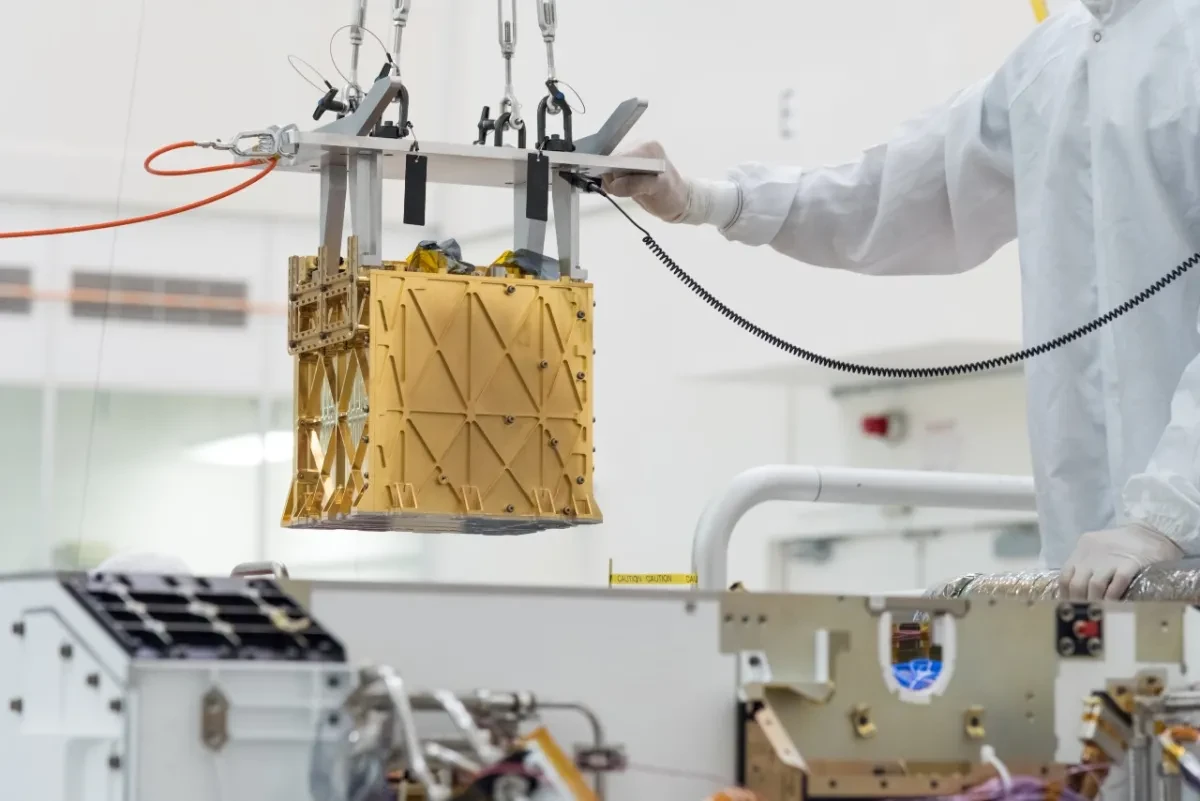 A gold-coloured, cube-shaped instrument is lowered into place in a NASA laboratory