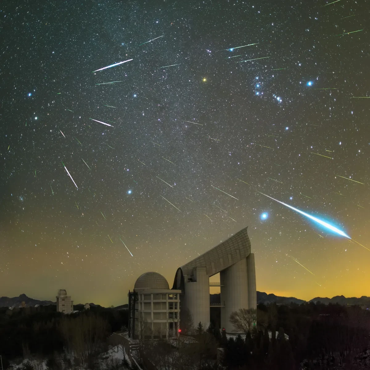 Image of meteor shower with around 30 meteors in the sky over a large observatory telescope