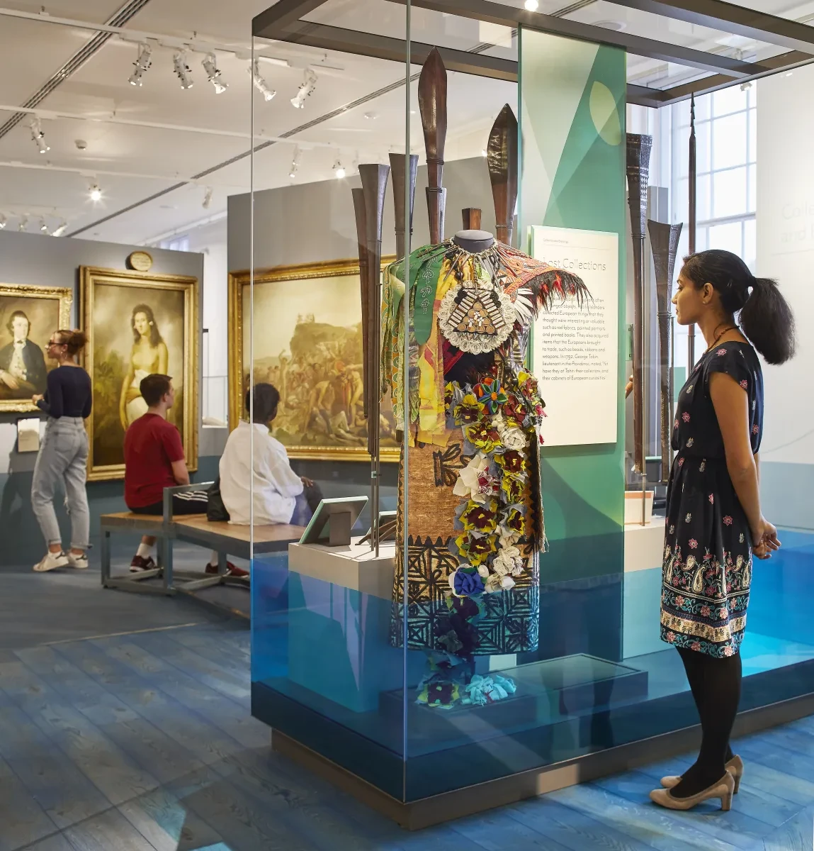 A woman looks at a dress displayed in a glass case inside the Pacific Encounters gallery.