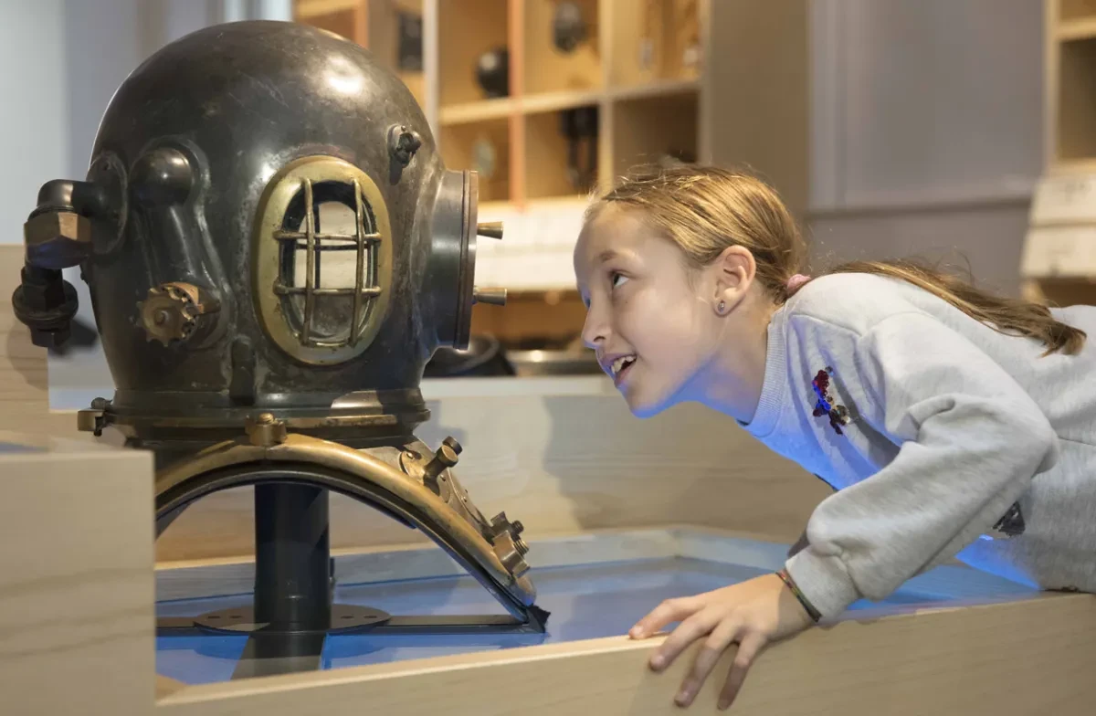 A young visitor looks at a diving helmet on display.