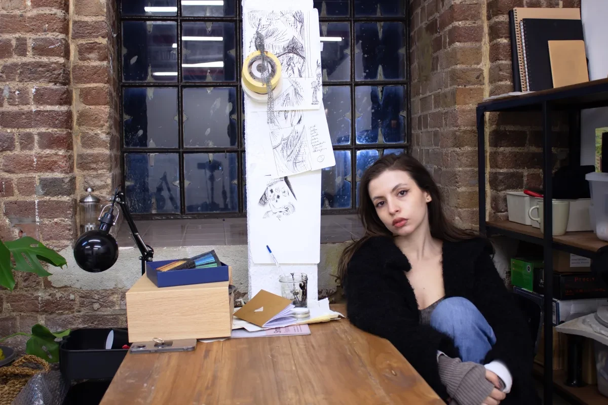 Livia Giorgina Carpineto sits in her studio in front of brick walls and an illustration